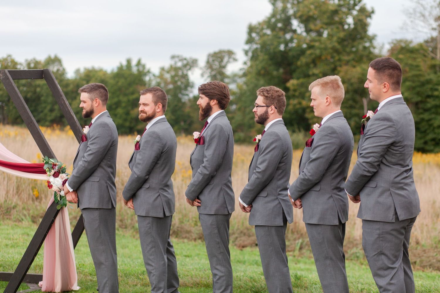 Groomsmen lined up in matching grey suits at outdoor wedding ceremony.