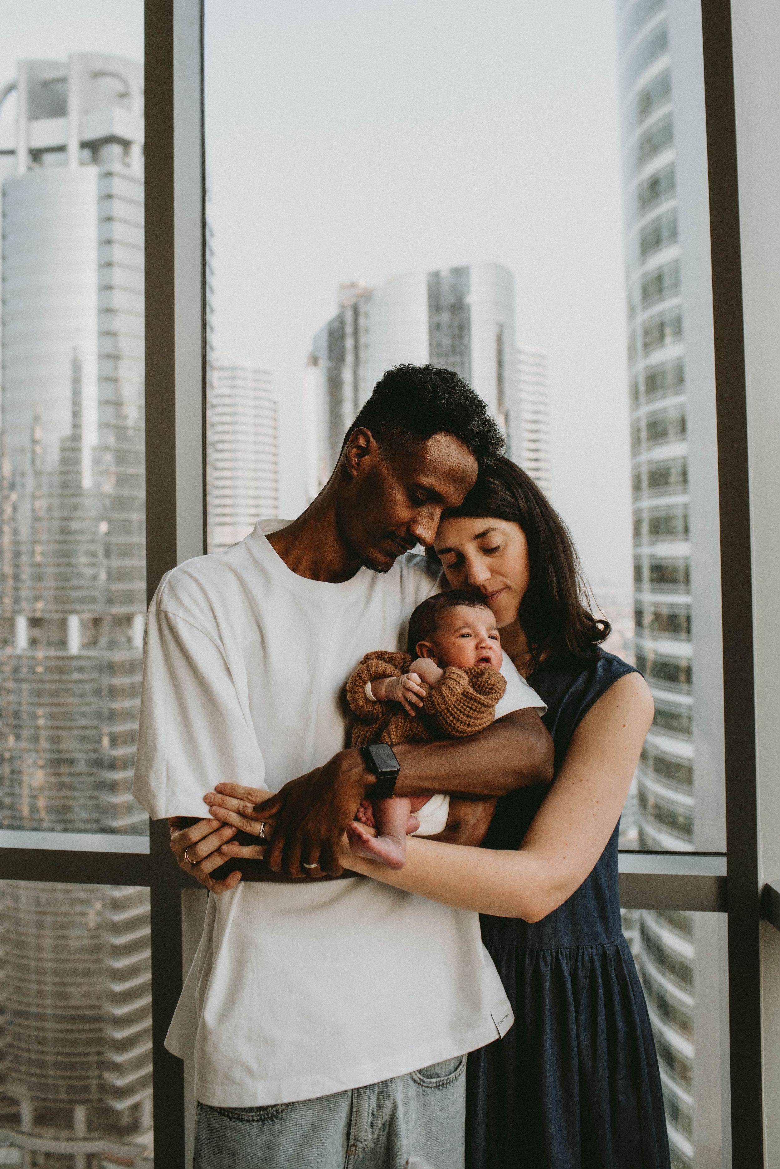 Mom, dad, and baby in a multiracial family portrait in Sydney, with the city skyline in the background, preserving joyful and loving memorie