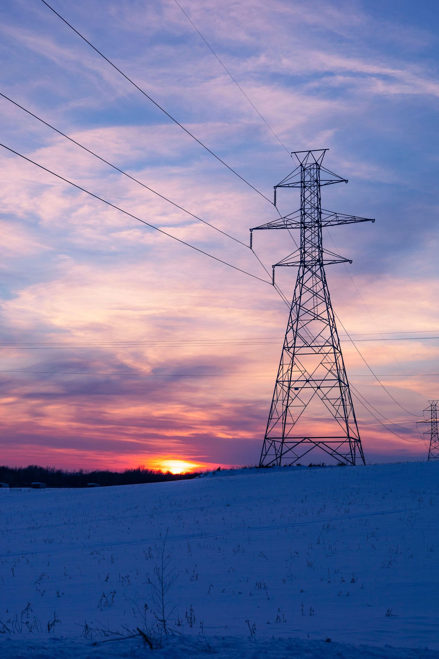 High voltage power line tower stands tall against a dramatic purple and orange sunset.