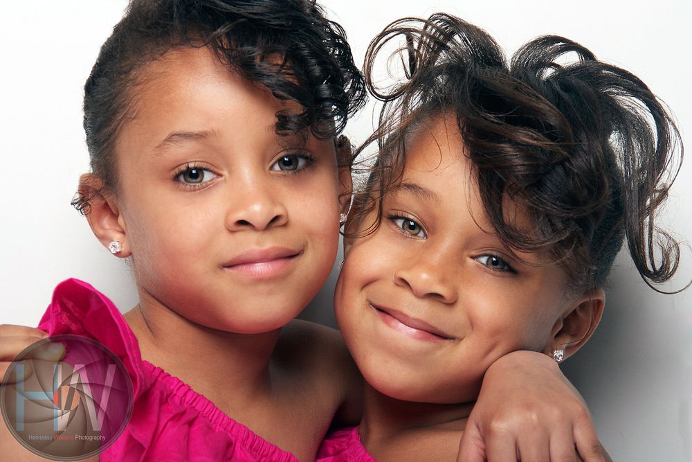 Close-up studio portrait of two young siblings in pink and black outfits against white background.