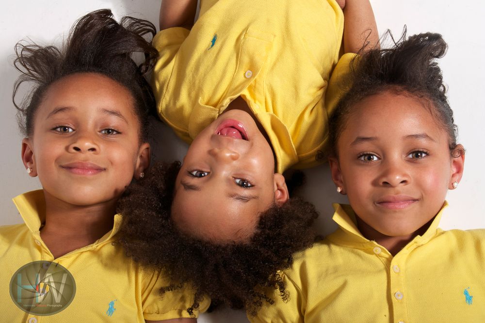 Three siblings in yellow shirts playfully posing together against white background.