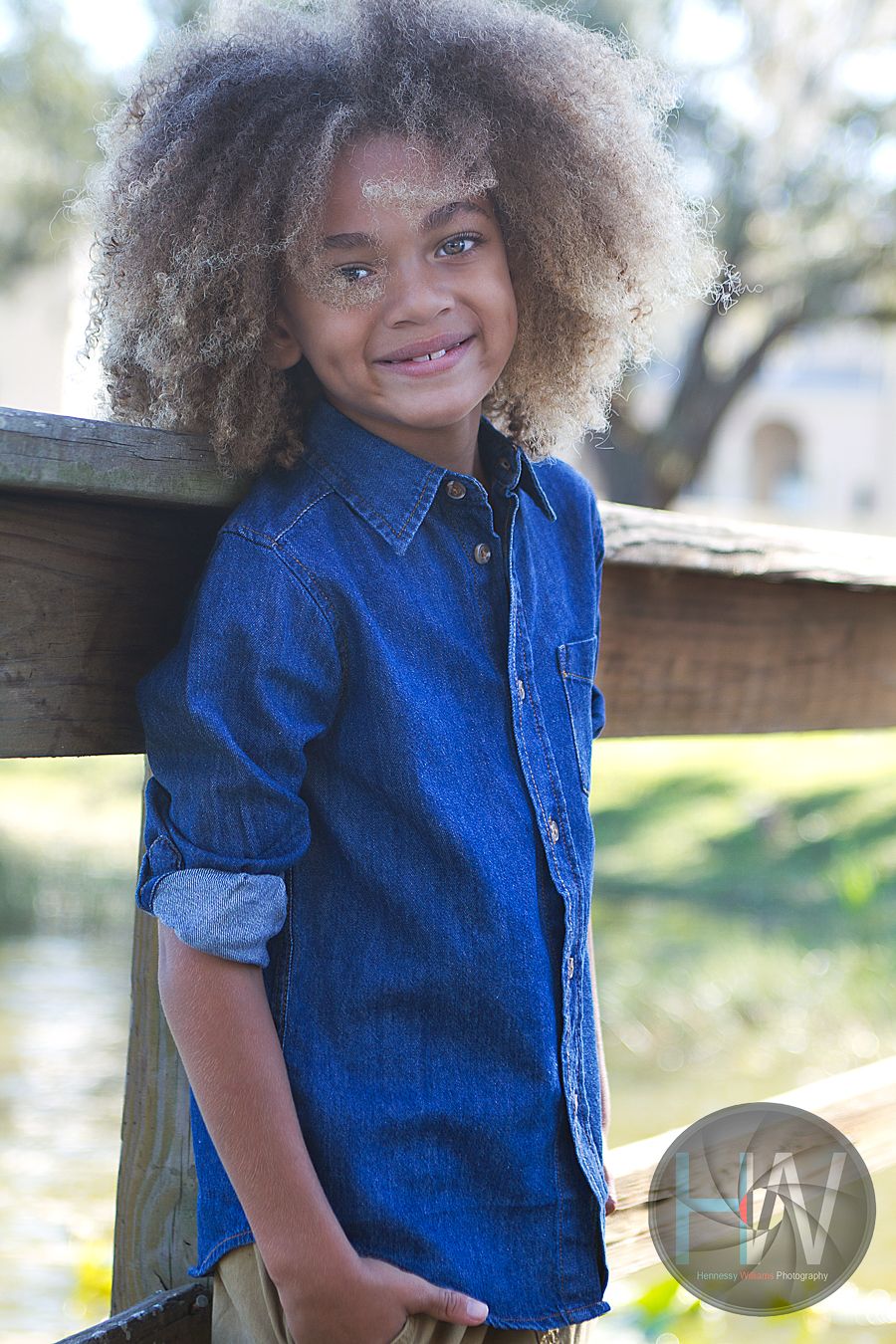 Young student in denim shirt smiling outdoors on wooden bench.
