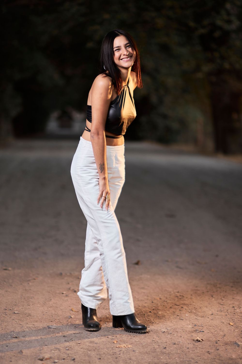 Full-length fashion shot of model wearing black crop top and white pants on dirt road.