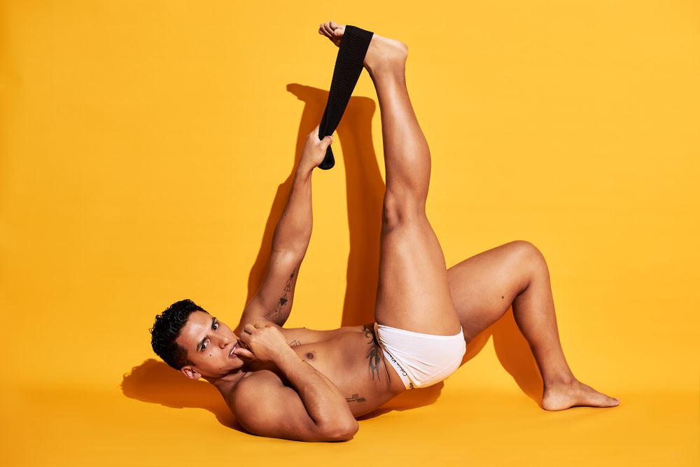 Artistic fitness photo with person stretching in white briefs against vibrant yellow background.