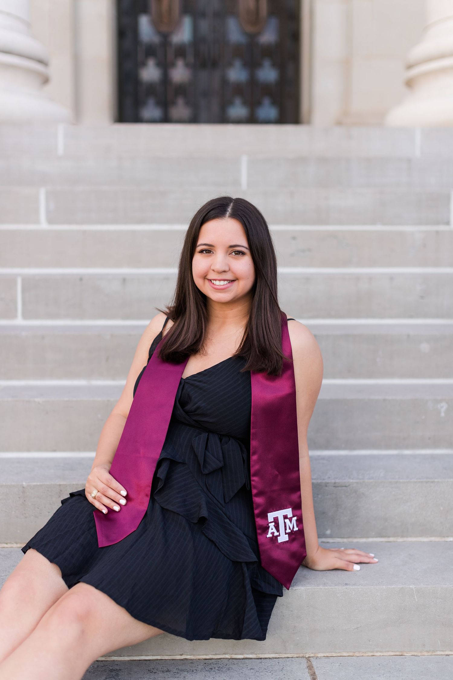 A graduation portrait on stone steps featuring maroon and black attire.