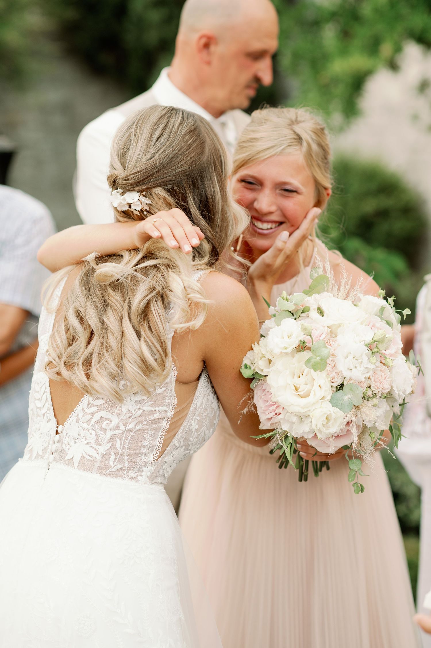 Two people share an emotional moment at a wedding while holding a bouquet of white flowers.