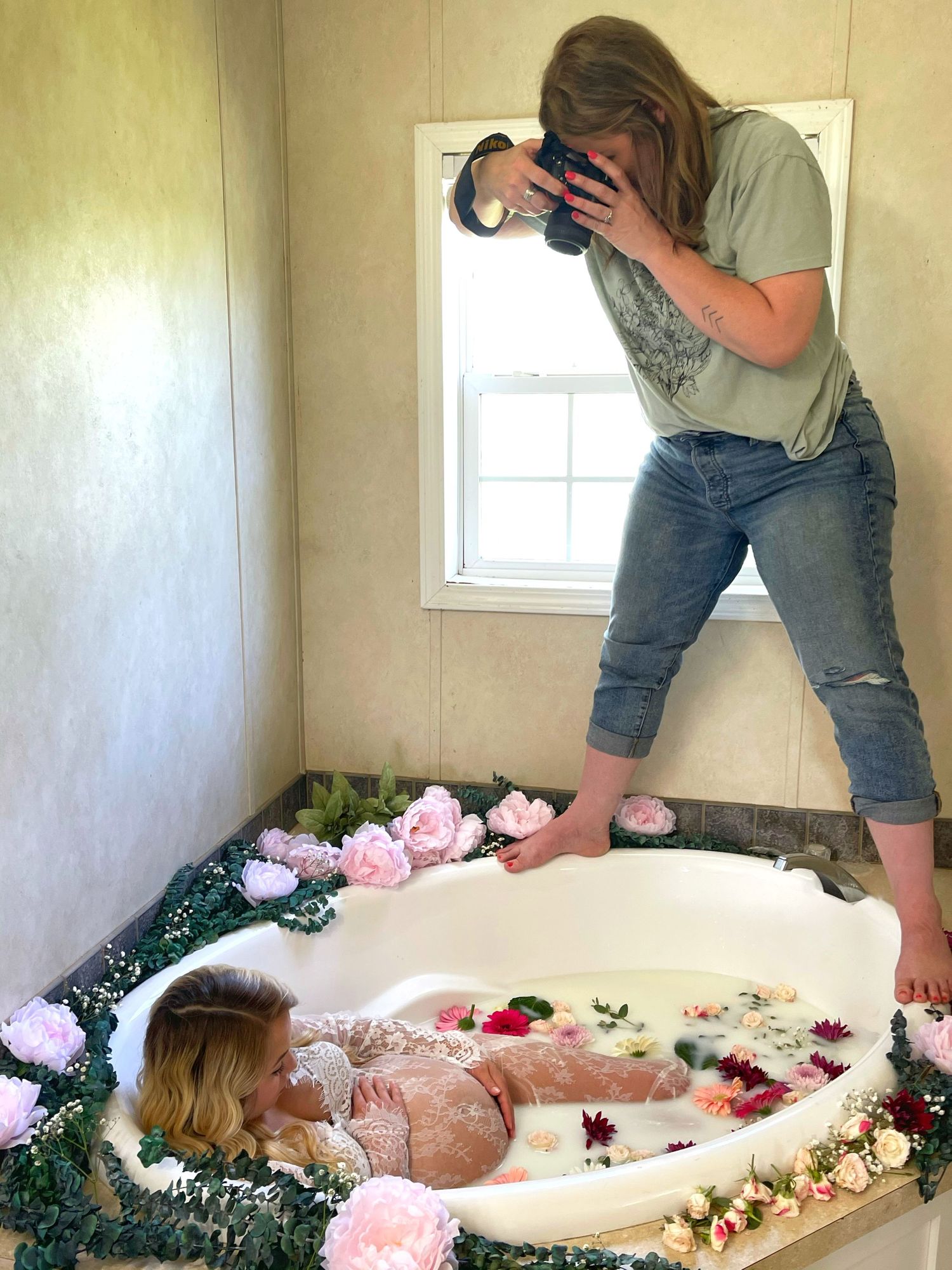 Behind-the-scenes view of milk bath photography session with camera and floral decorations.
