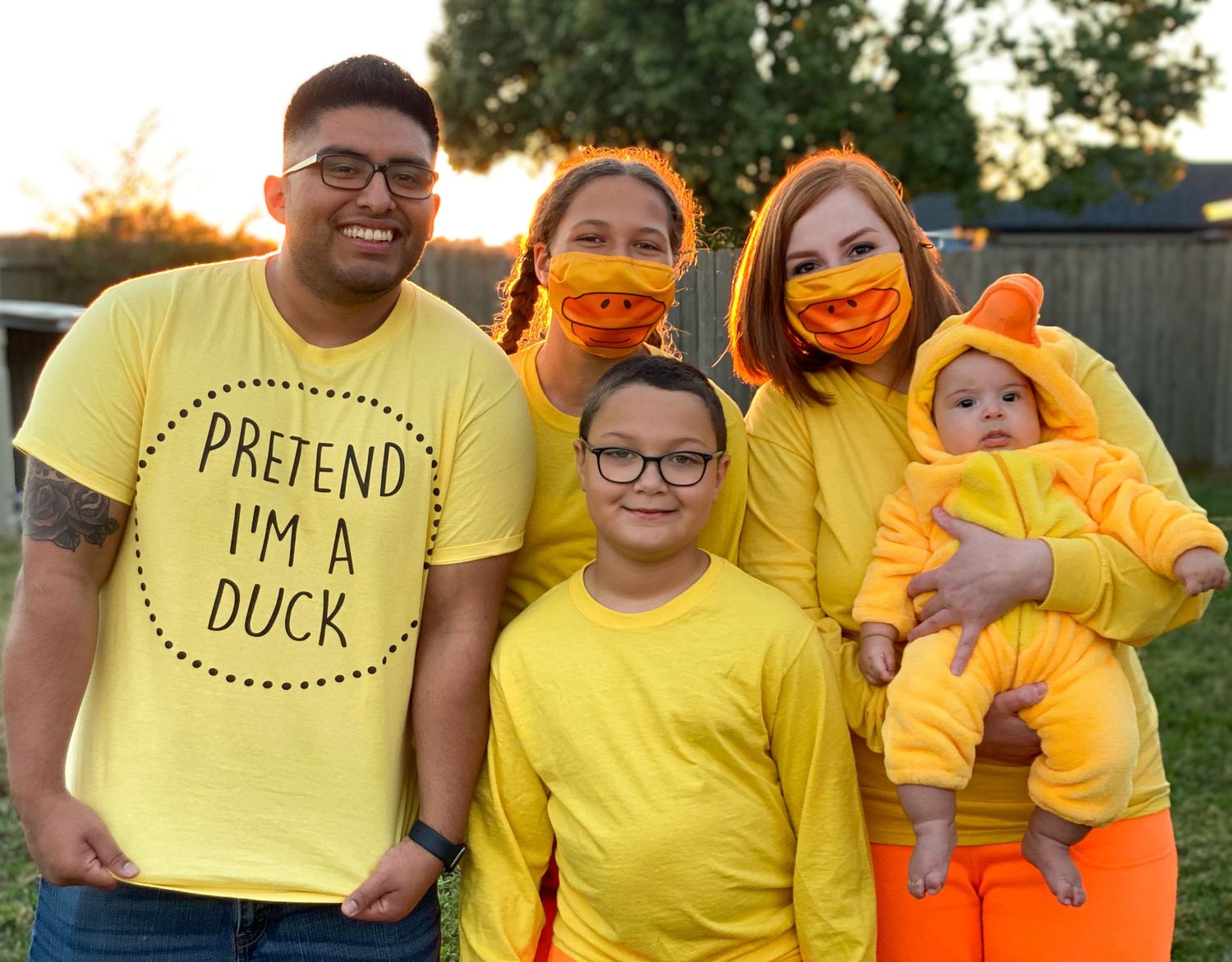 Family wearing yellow and orange duck-themed outfits poses together at sunset.