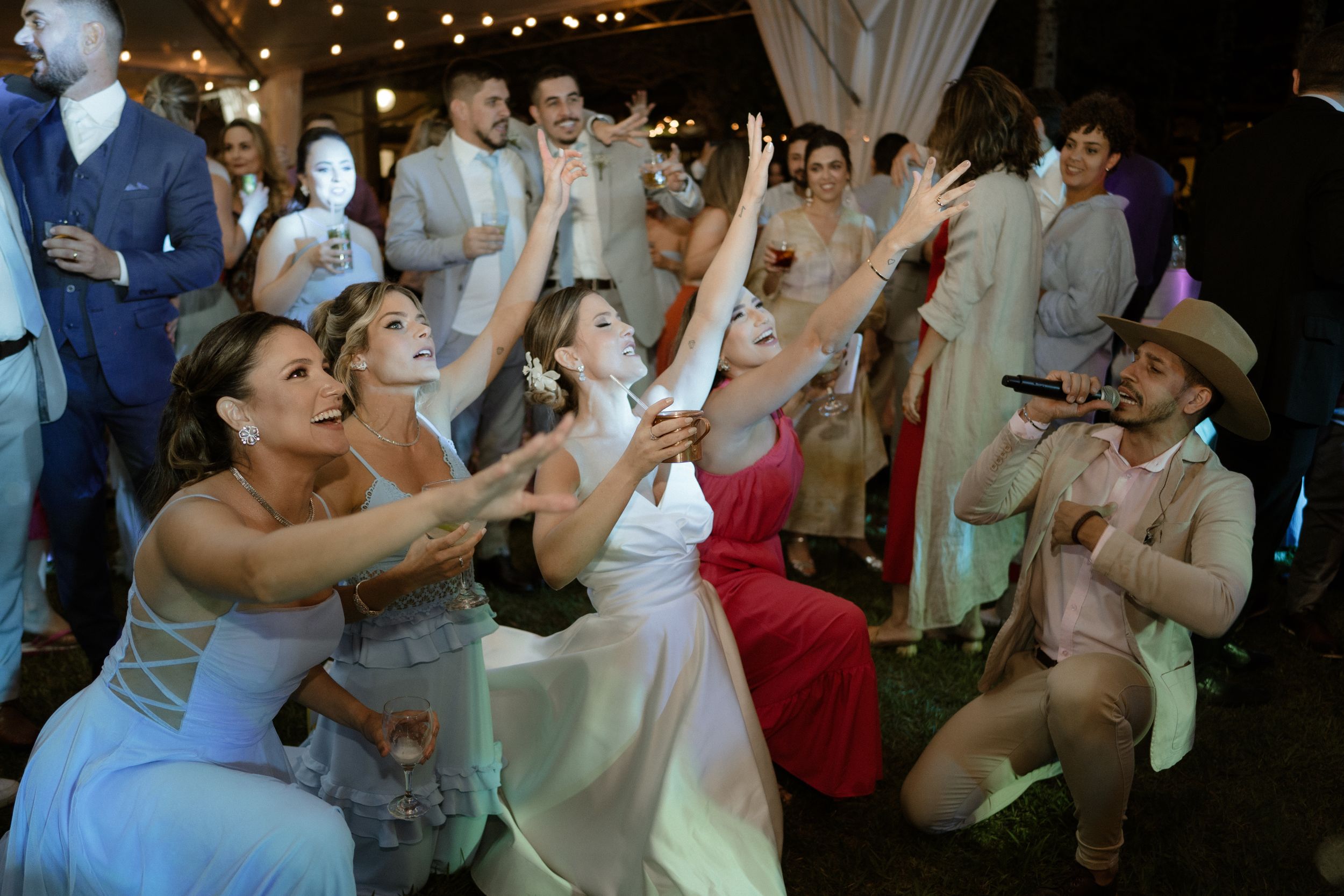 Wedding guests dance enthusiastically with raised arms during outdoor celebration.