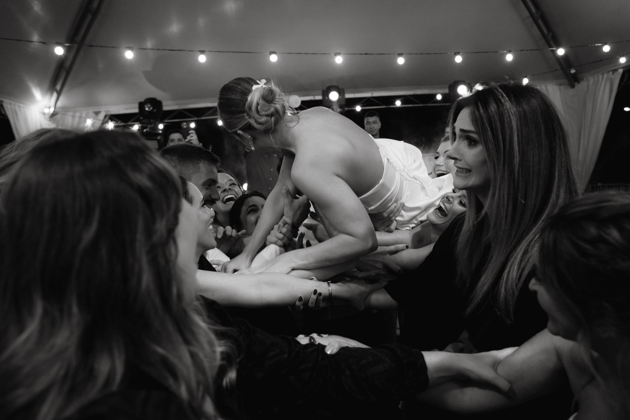 Black and white photo of wedding celebration with guests dancing in crowded tent.
