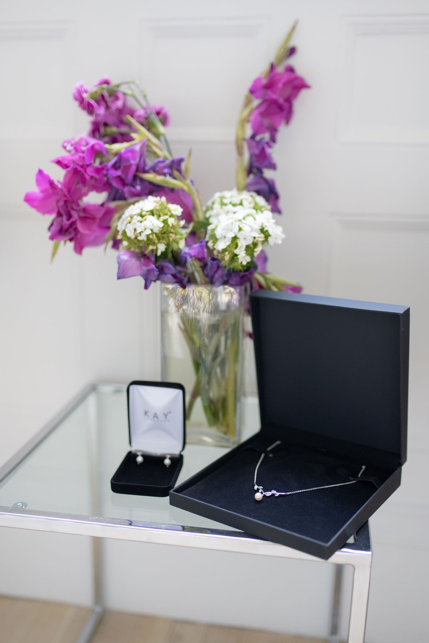 Elegant floral arrangement with purple flowers next to jewelry boxes on a glass table.
