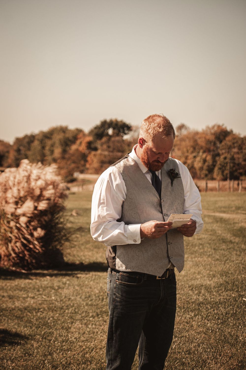 Person in gray vest reading personal letter in autumn field setting.