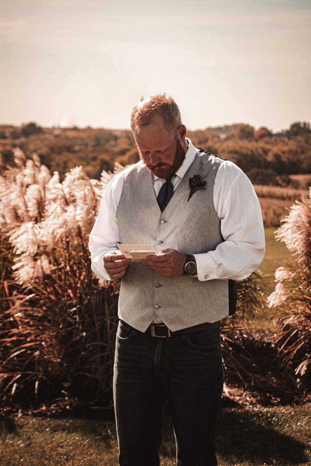 Person in formal attire reading from paper while standing in field of pampas grass.