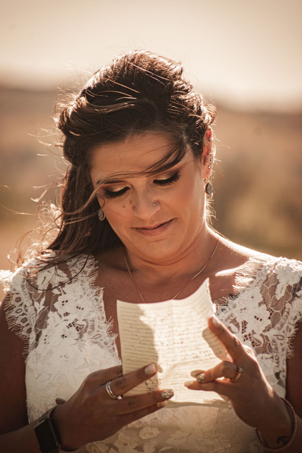 Emotional bride reading heartfelt letter outdoors in warm sunlight wearing delicate lace wedding dress.