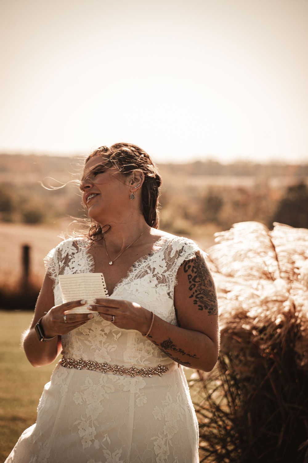 Joyful bride laughing while holding letter outdoors in romantic sunset lighting.