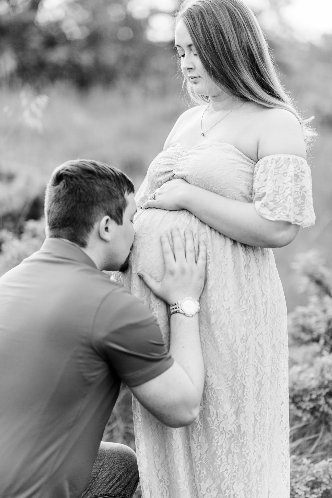 Maternity session with dad kissing mom's tummy in field in golden hour sunlight at Moraine State Park, Pennsylvania