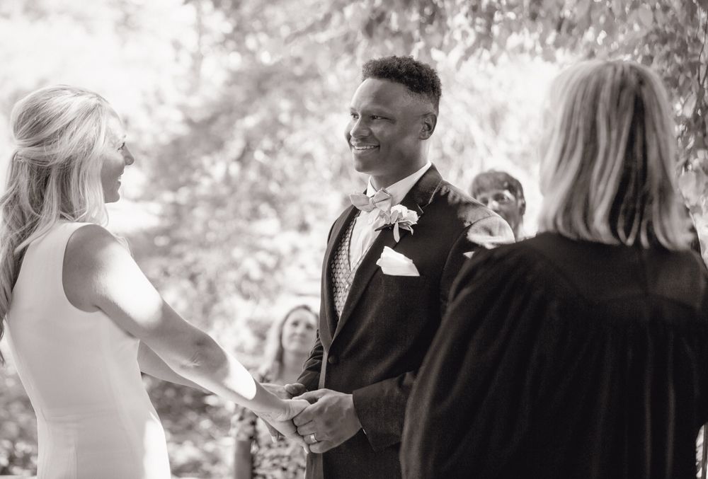 Black and white wedding ceremony photo showing guests sitting in rows outdoors.