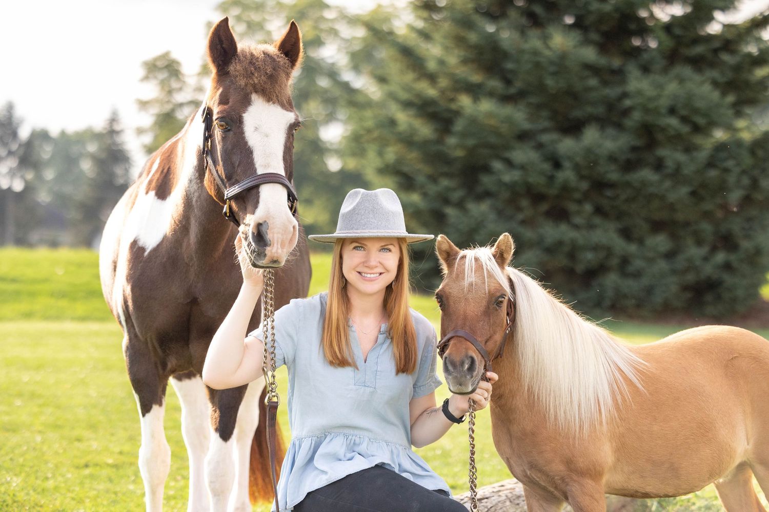 Emily sitting on a log while holding her paint pony and mini