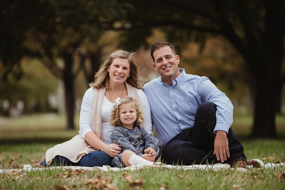 A relaxed outdoor family portrait session on fallen leaves in an autumn park setting.