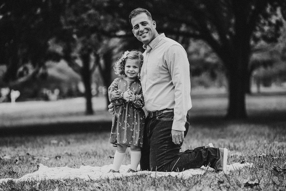 Black and white portrait of family members sharing a tender moment in a park setting.
