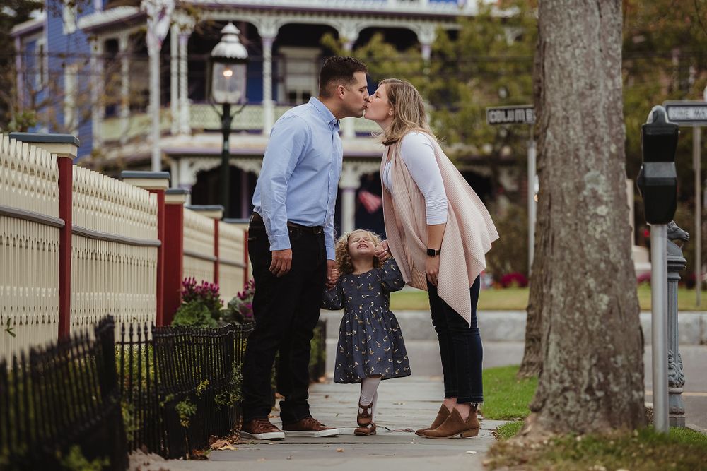Sweet family moment captured on sidewalk with Victorian architecture in background.