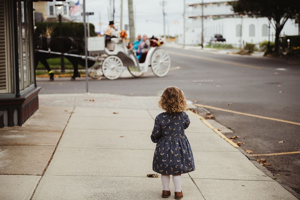Young child in navy dress looking at vintage carriage on city sidewalk.