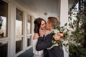 A romantic wedding moment captured on a white porch with a bouquet of pink flowers.