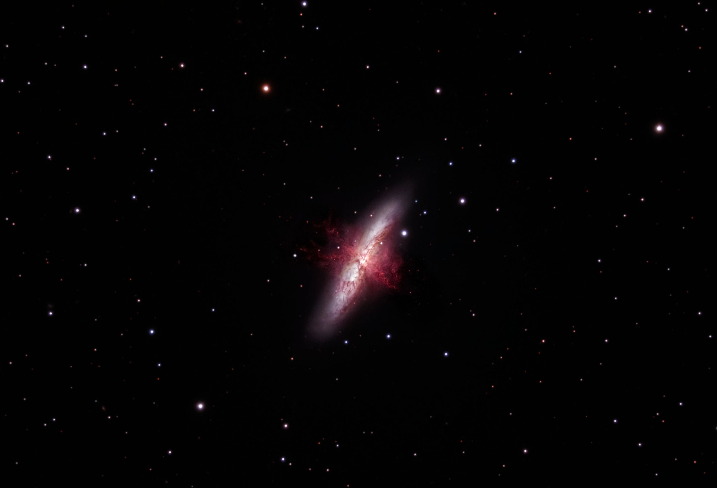 A distant galaxy glows with a reddish hue as it stretches diagonally across the star-filled frame.