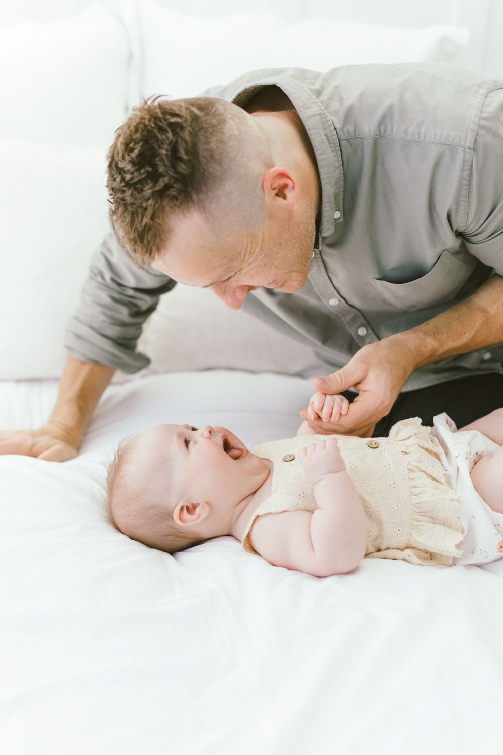 Adult sharing joyful moment with baby on white bedding.