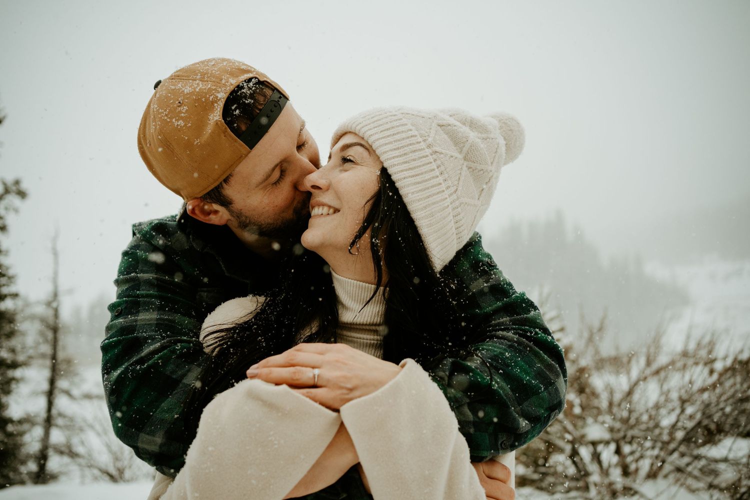 Couple in winter attire sharing an intimate moment against a snowy backdrop.