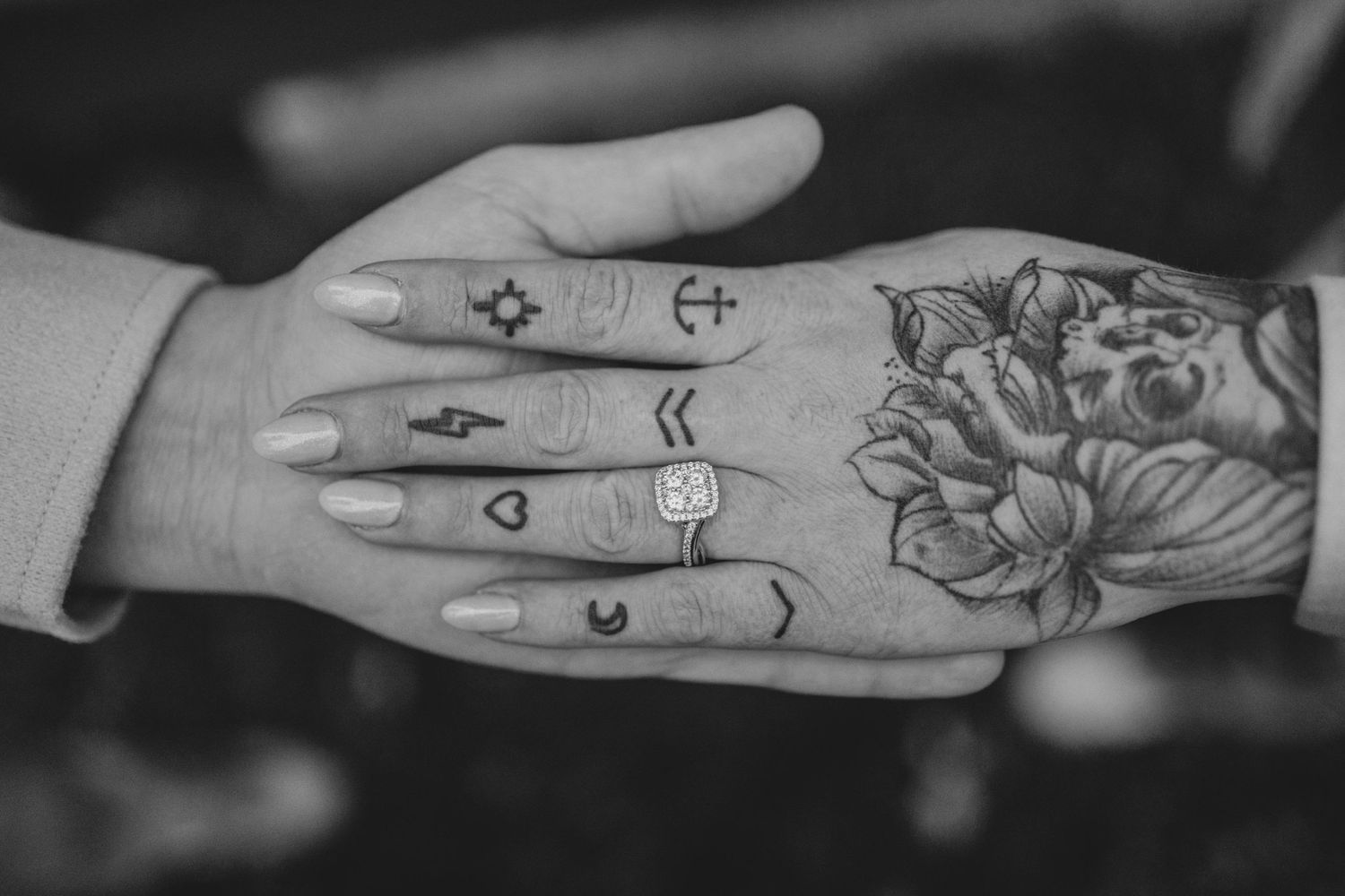 Close-up of tattooed hand with geometric symbols and floral design in black and white for an engagement session.