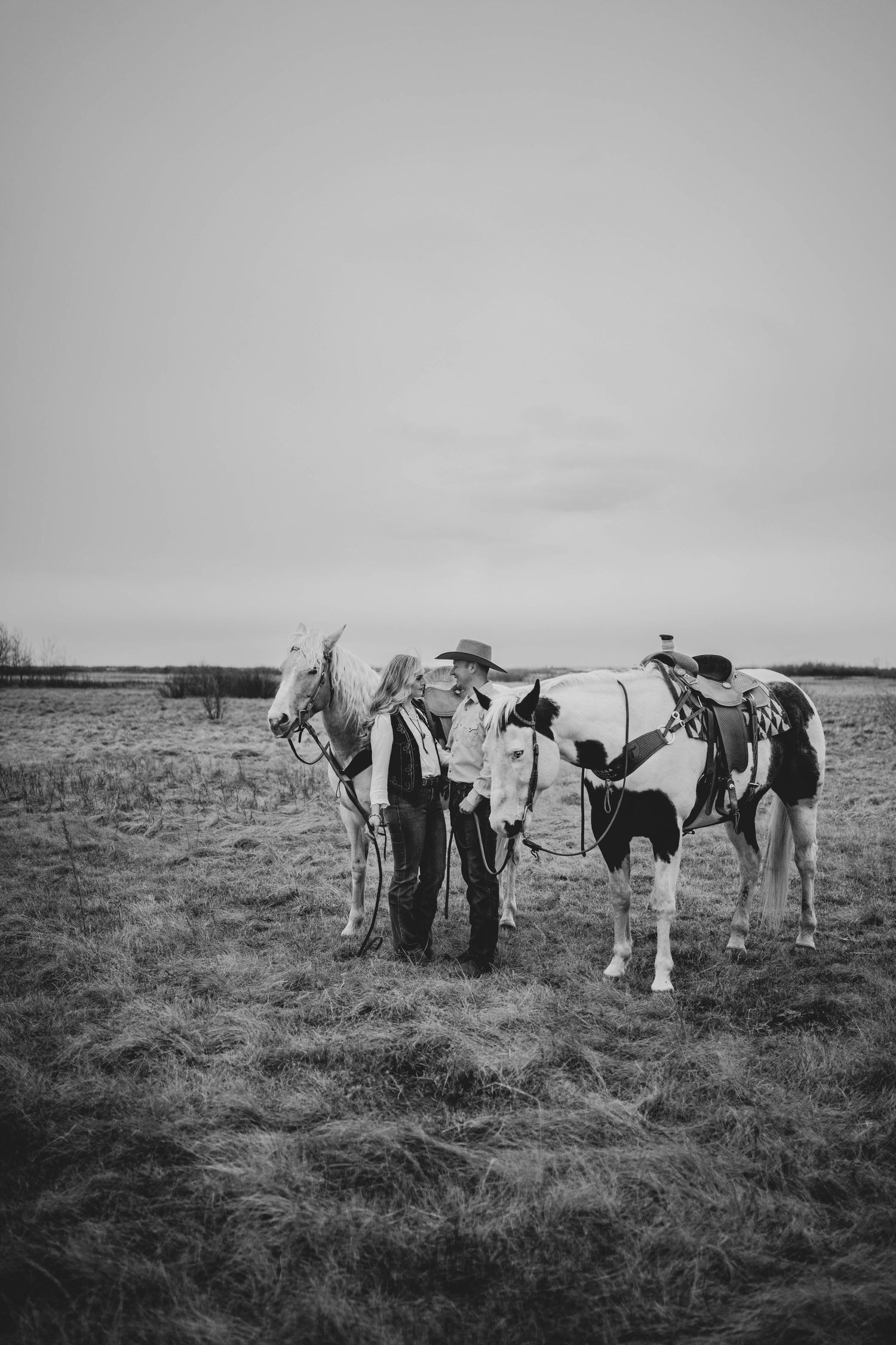 Black and white photo of a group gathered with their horses in a rural field.
