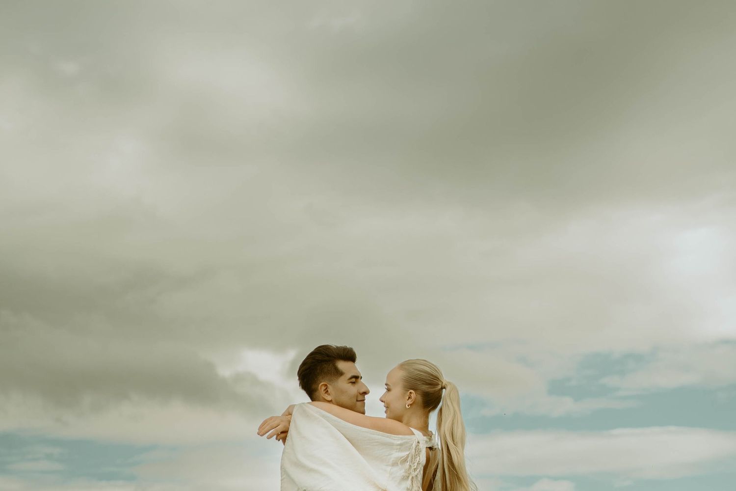 A joyful embrace under cloudy skies with white fabric flowing in the wind in Iceland.