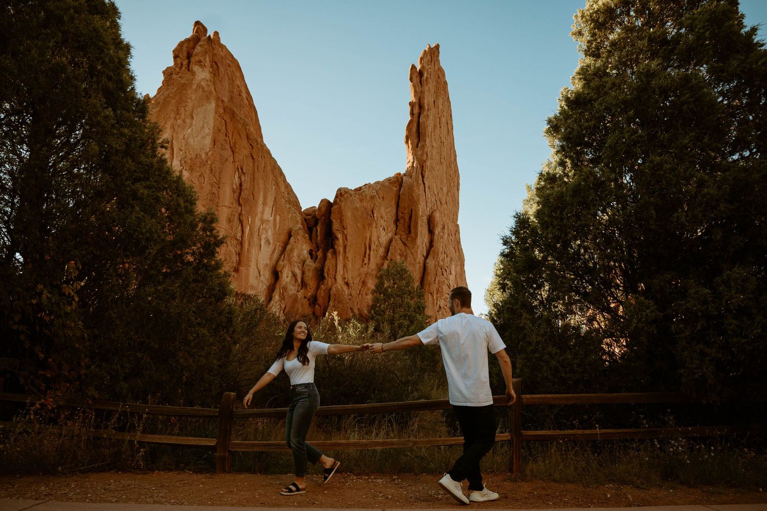 A couple jumps playfully in front of towering red rock formations at sunset in Colorado.