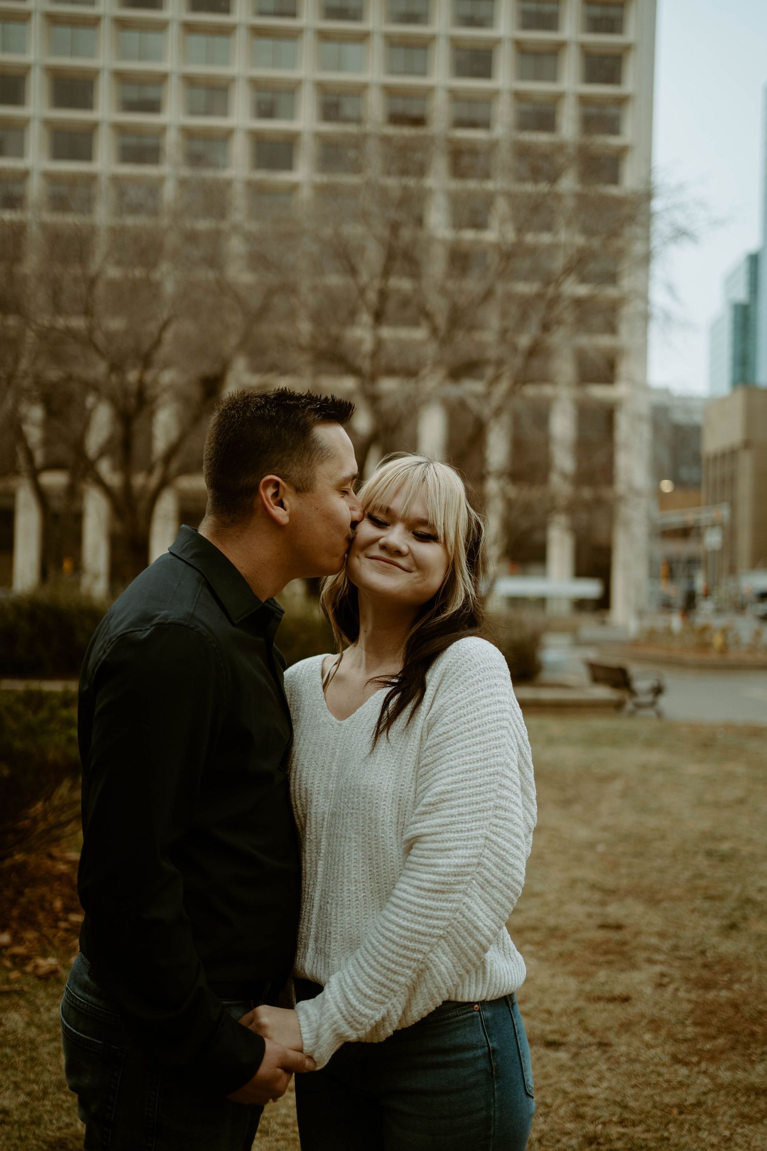 Tender moment captured between couple in casual winter wear against urban backdrop.