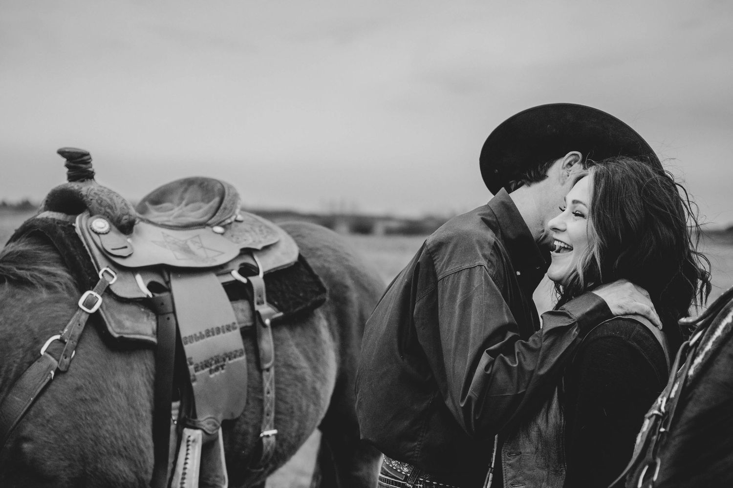 Black and white western romantic scene with horses and saddles in the background.