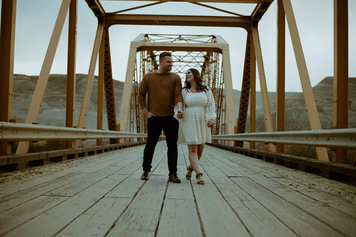 Couple standing together on wooden bridge at sunset.