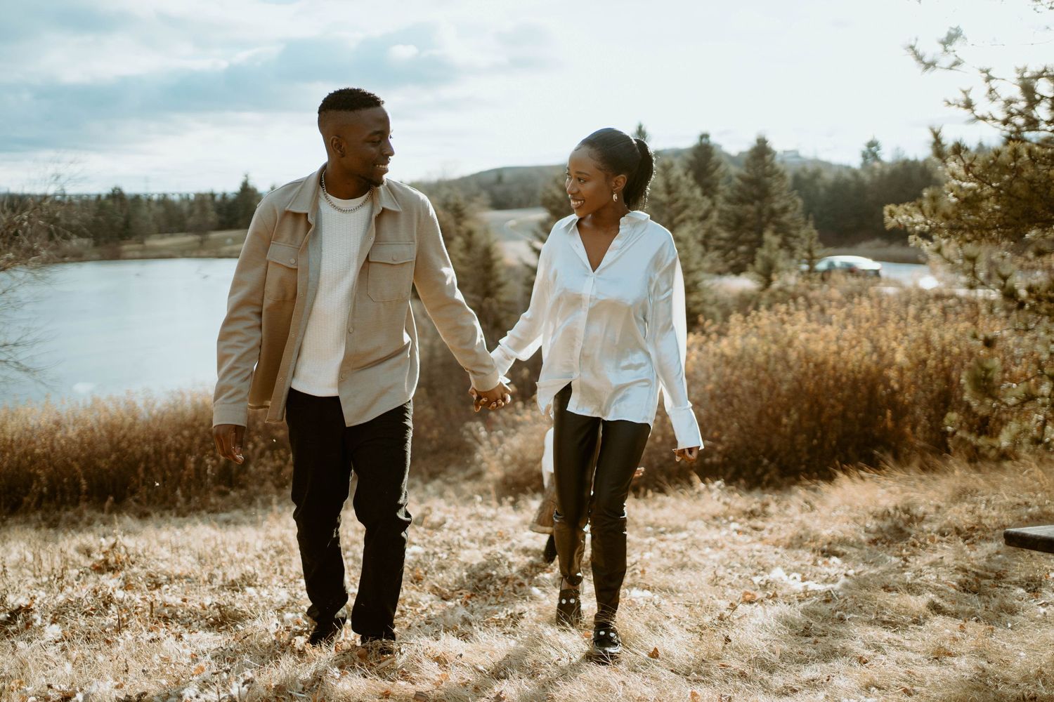 Couple holding hands while walking along a scenic lakeside trail on a sunny day.