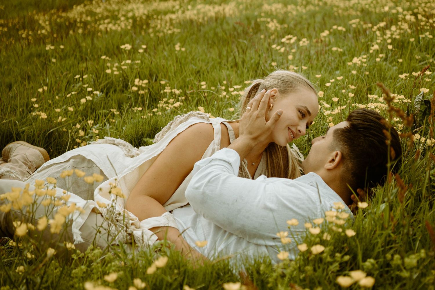 Romantic couple lying in meadow of yellow wildflowers on sunny day in Iceland.