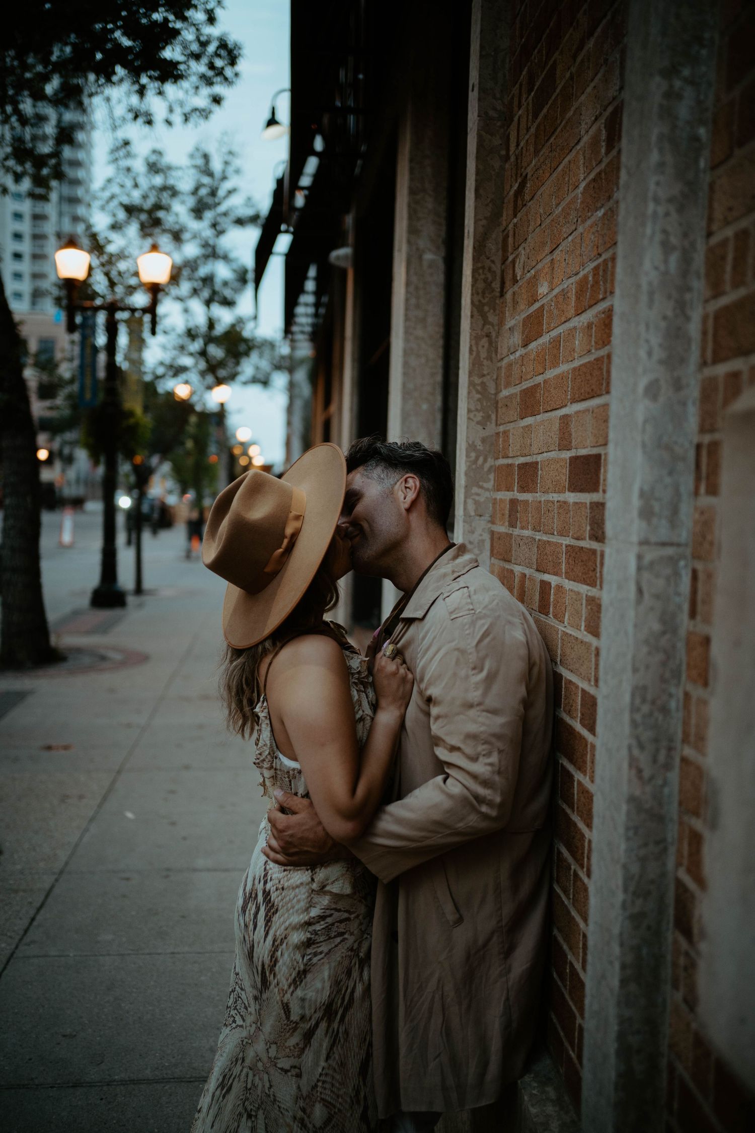 A romantic urban photo of a couple embracing against a brick wall at twilight.