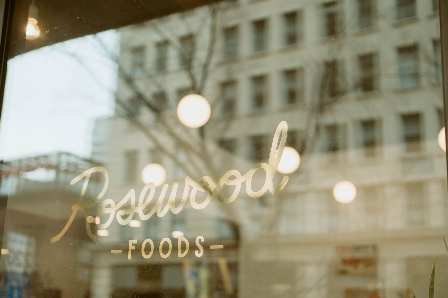 Rosewood Foods storefront window with vintage food sign and glowing lights.
