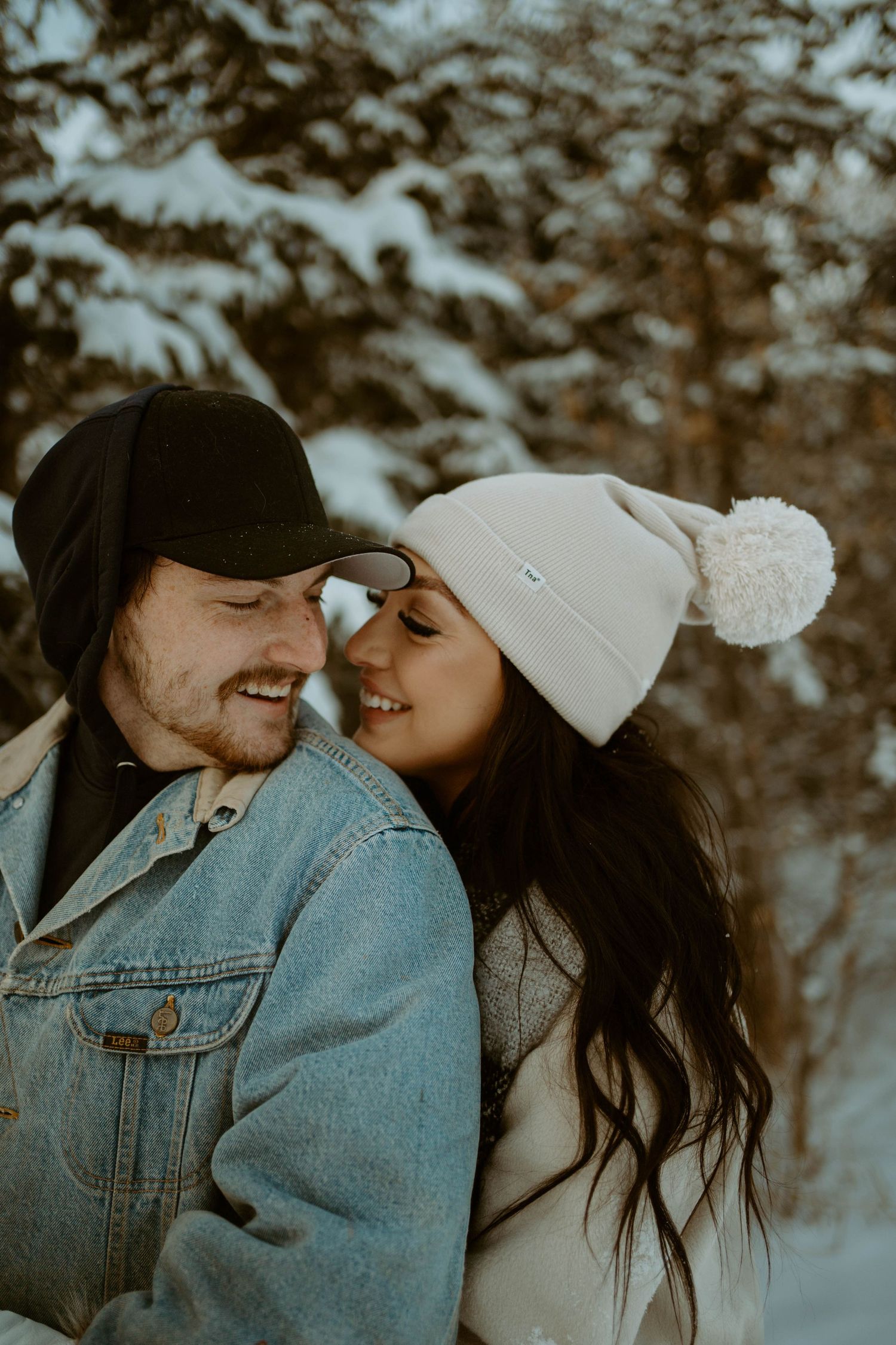Cozy winter portrait of a couple in denim jacket and knit hat sharing an intimate moment in a snowy setting.