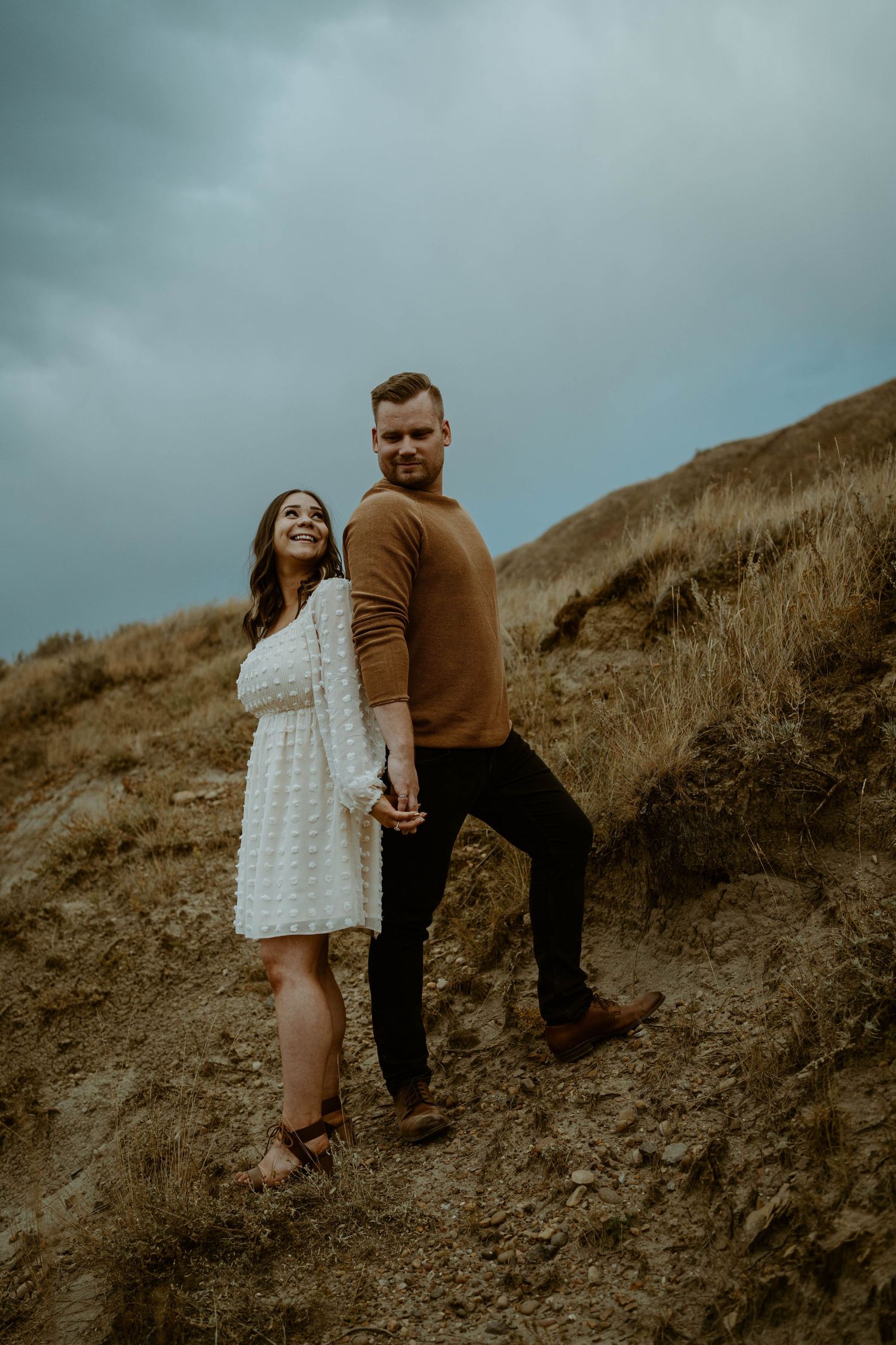 Couple in casual attire standing on hillside during moody overcast day.