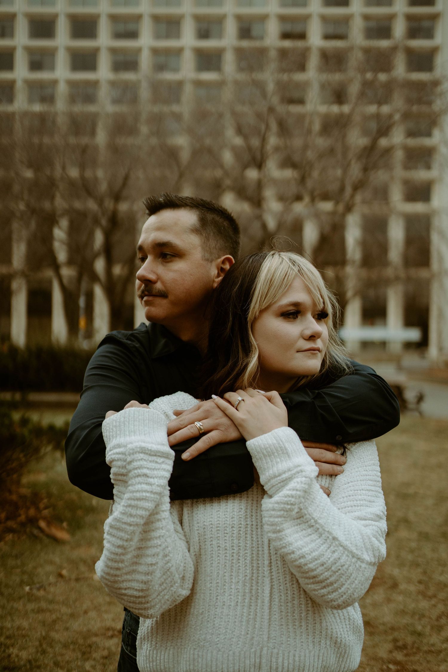 Intimate portrait of couple embracing in chunky knit sweaters against city backdrop.