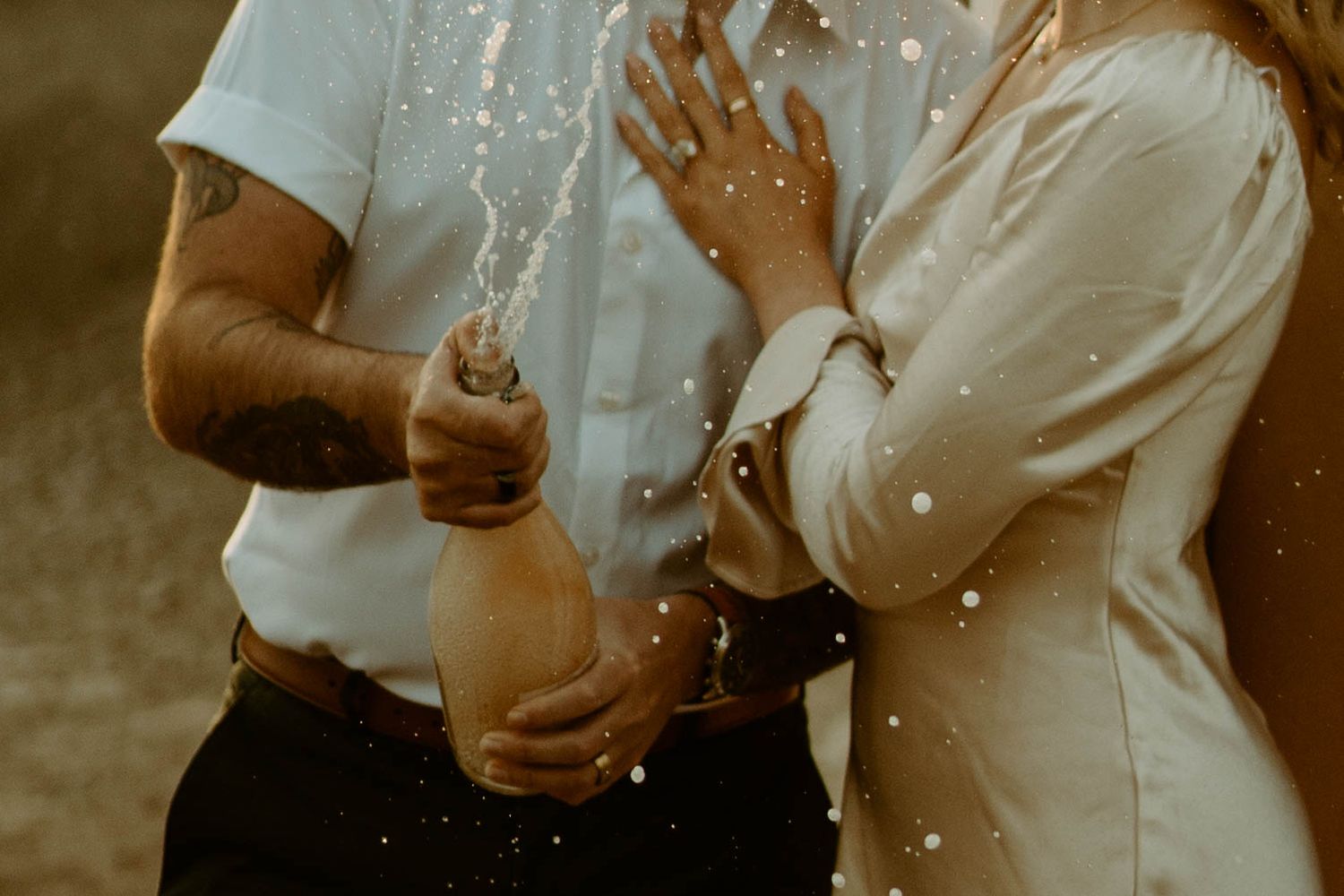 Champagne spraying during a romantic celebration with sparkling droplets in golden sunlight.