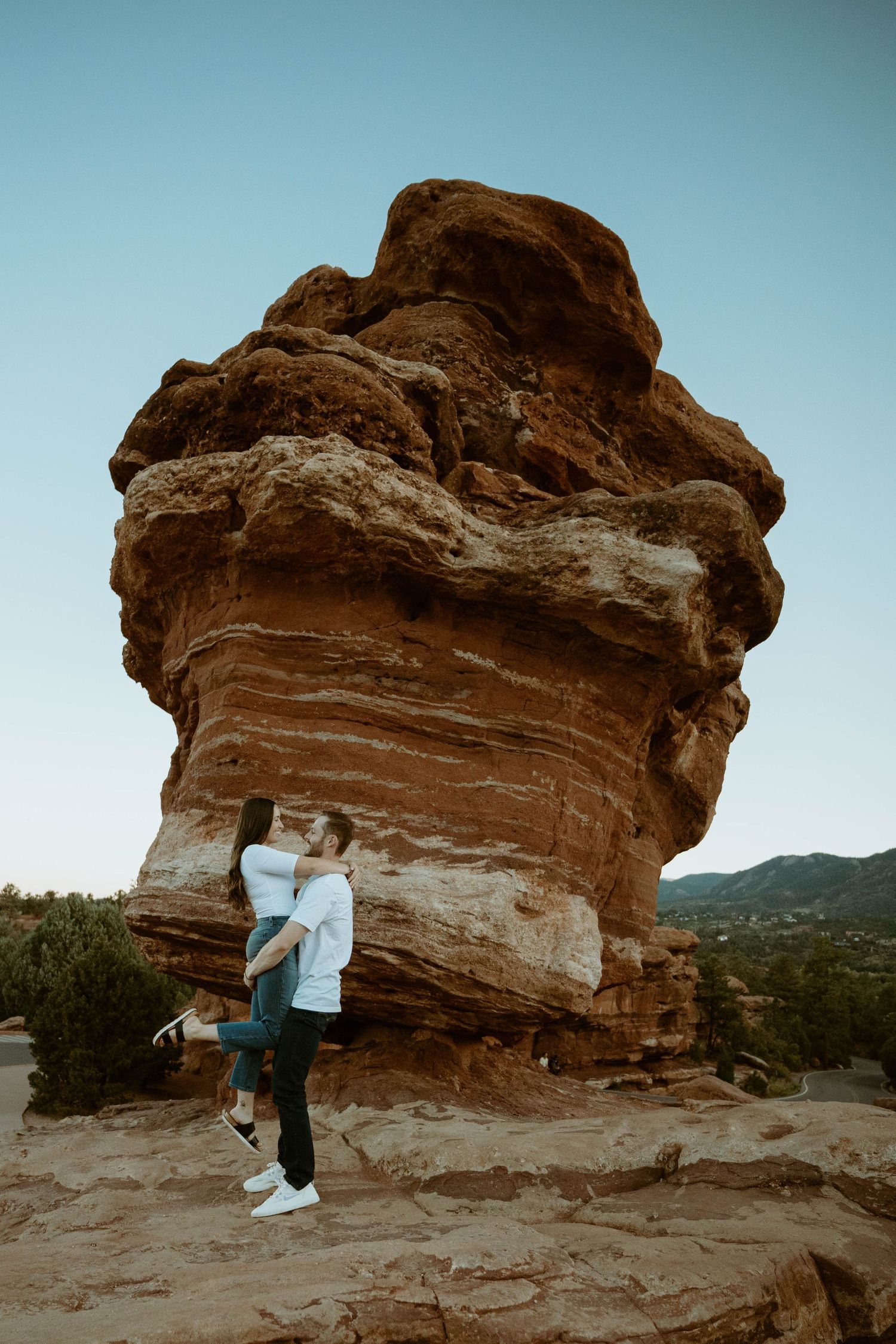 A couple embraces in front of a unique mushroom-shaped rock formation in warm evening light in Colorado.