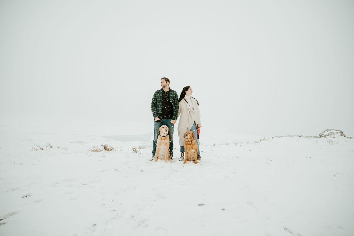Couple standing together on a snow-covered hilltop in winter conditions.