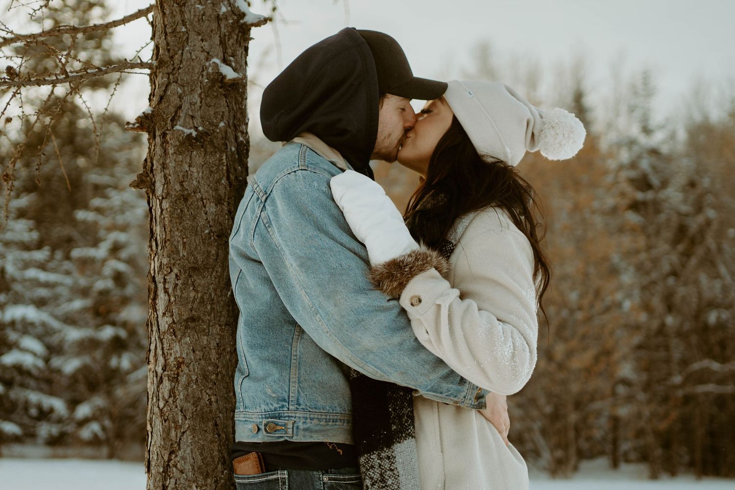 Intimate winter scene of couple embracing by pine tree in snow.
