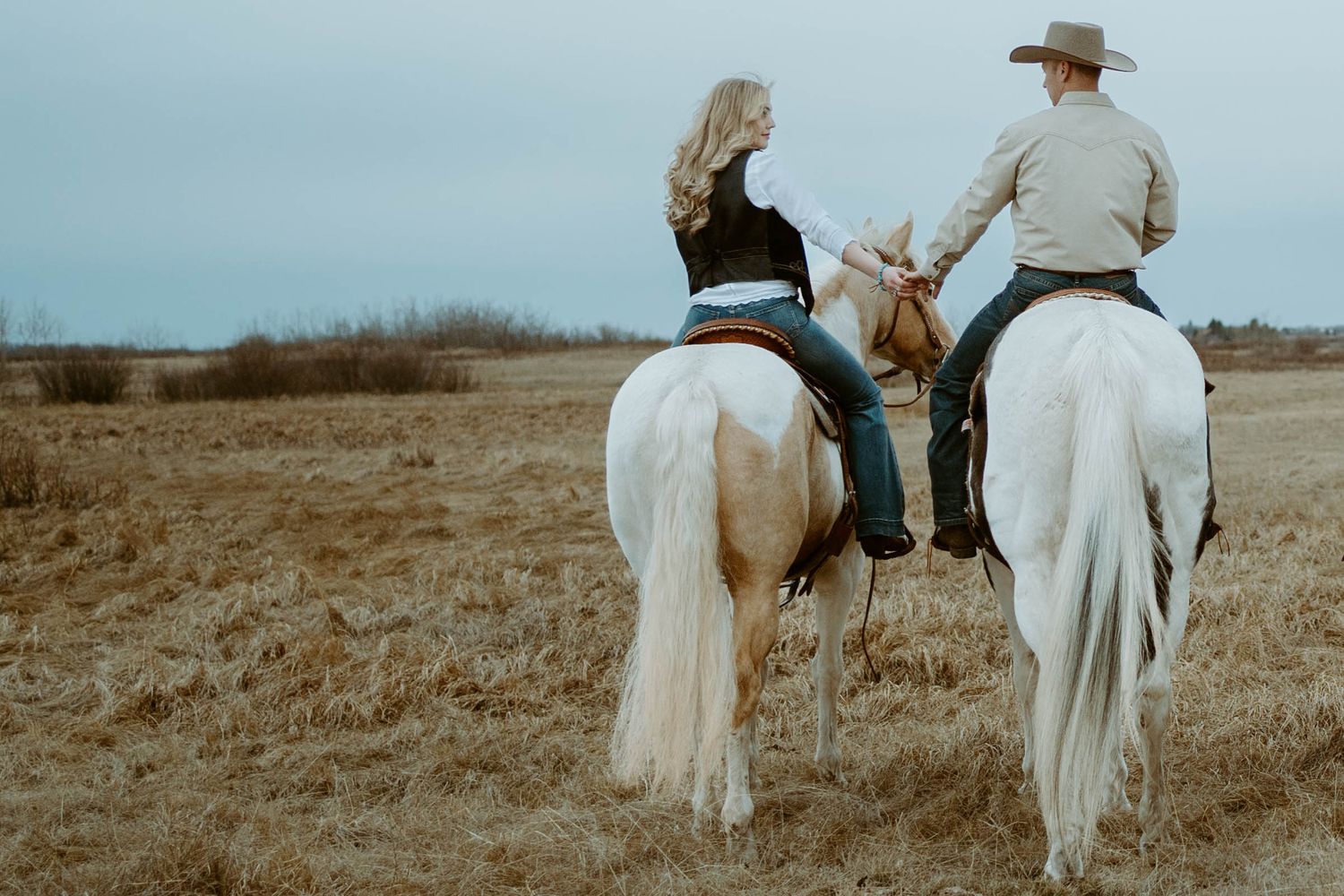 Two riders on white horses travel together across an open field.