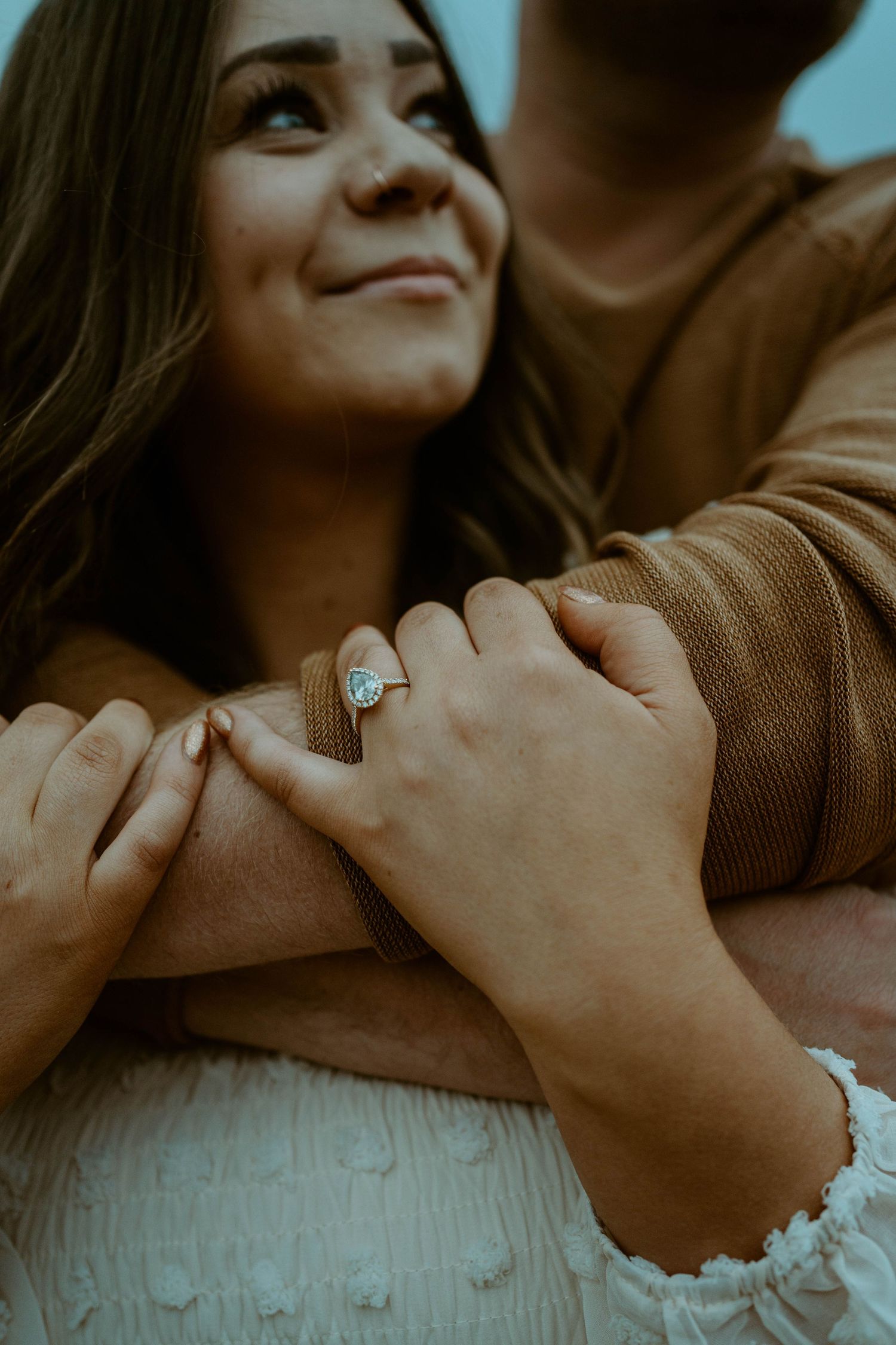 Close-up shot of embracing couple showing engagement ring against cloudy backdrop.